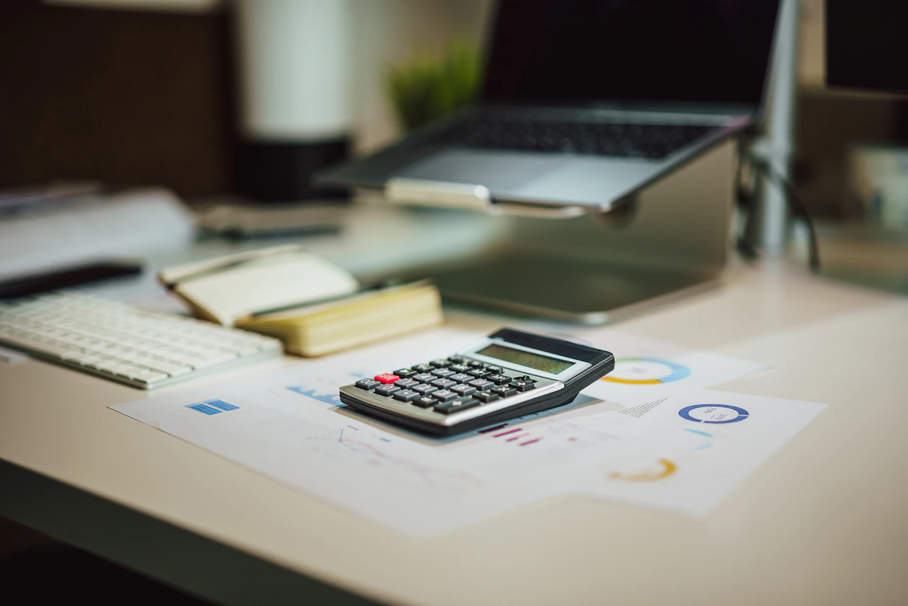 Calculator on printed financial charts beside a notebook and computer