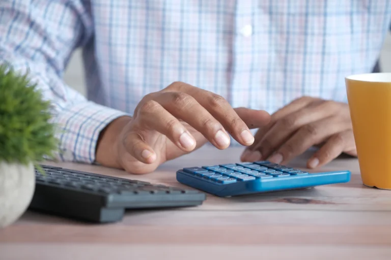 Person using a blue calculator beside a laptop on a desk