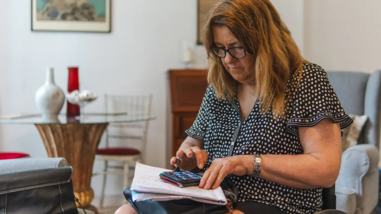 Woman using a calculator beside financial paperwork at a desk