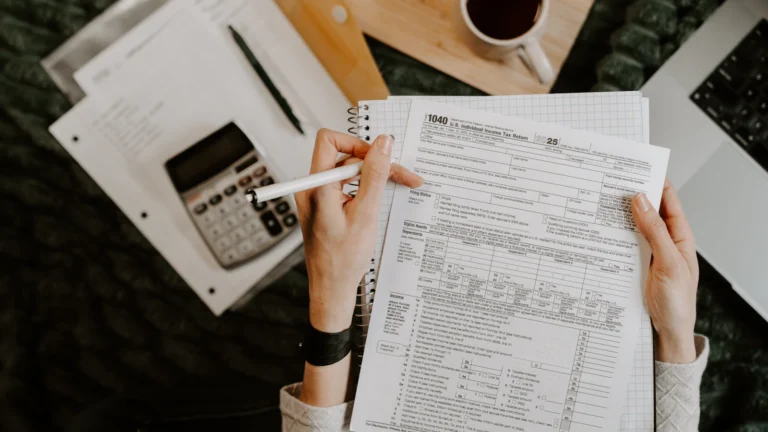Person reviewing printed financial documents beside a laptop and calculator at a desk