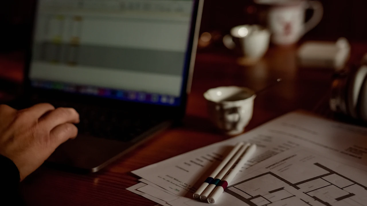 Person using a laptop beside printed floor plans and pens