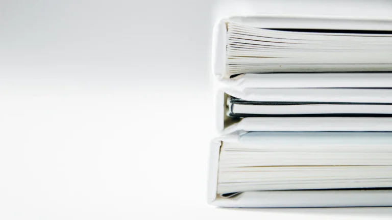 Three white-bound books stacked on a light surface