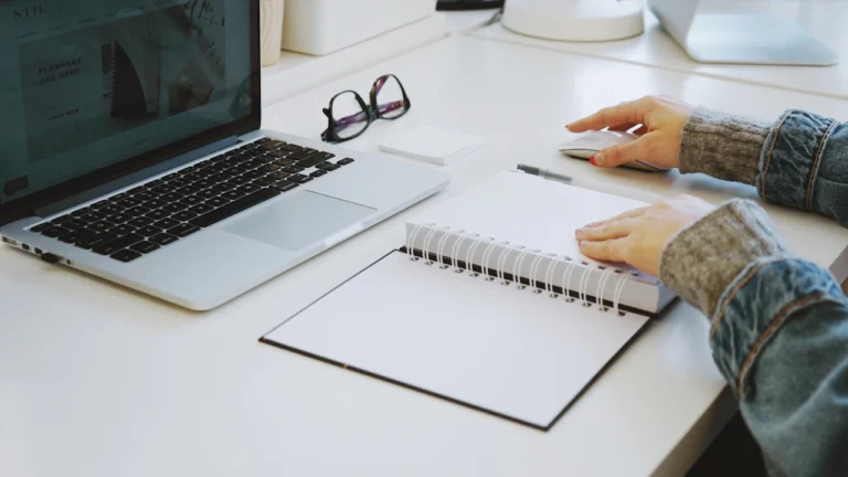 Person using a laptop beside an open notebook