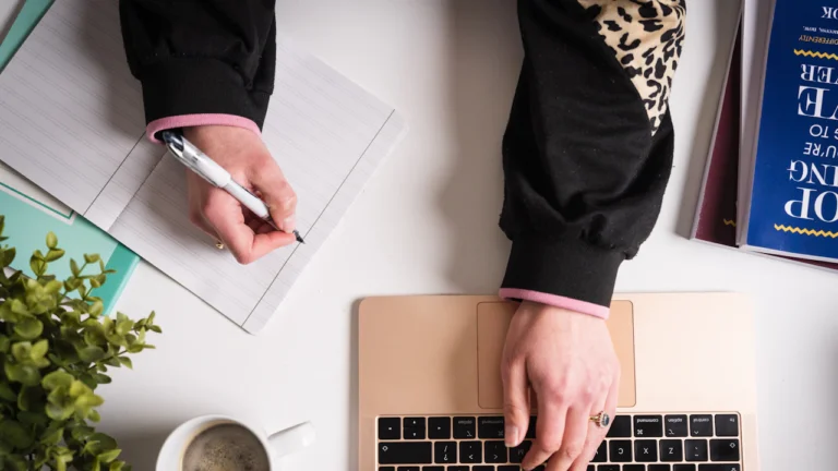 Person writing notes beside a laptop